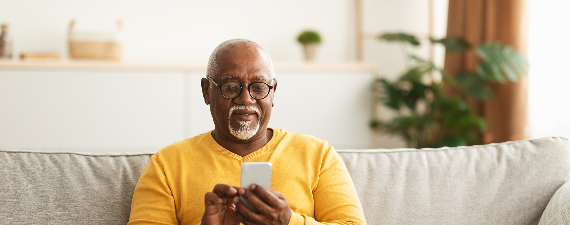 Senior Black Man Using Smartphone Texting Sitting At Home